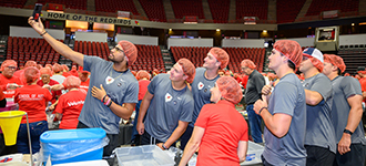 A group of students wearing red hairnets taking a selfie in an arena setting.